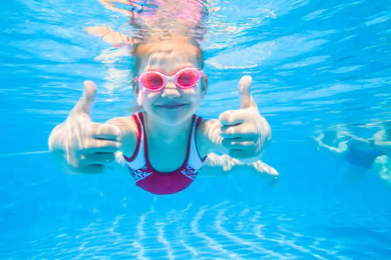 Girl wearing pink water glasses giving thumbs up underwater