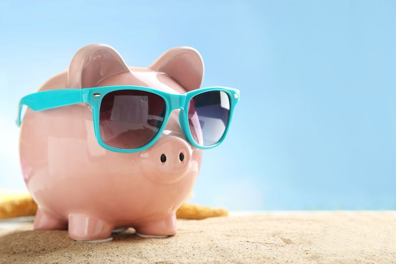 Piggy bank wearing sunglasses on a sandy surface