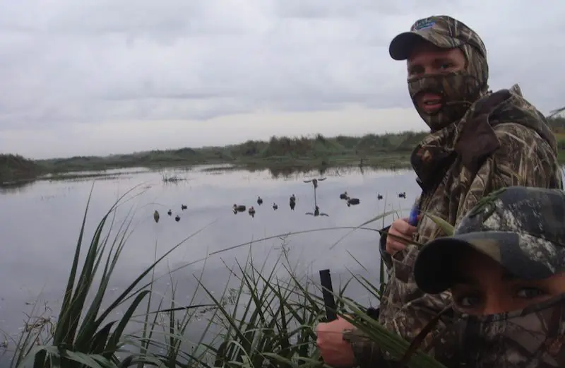 Man dressed in camouflage outfit by a lake when duck hunting