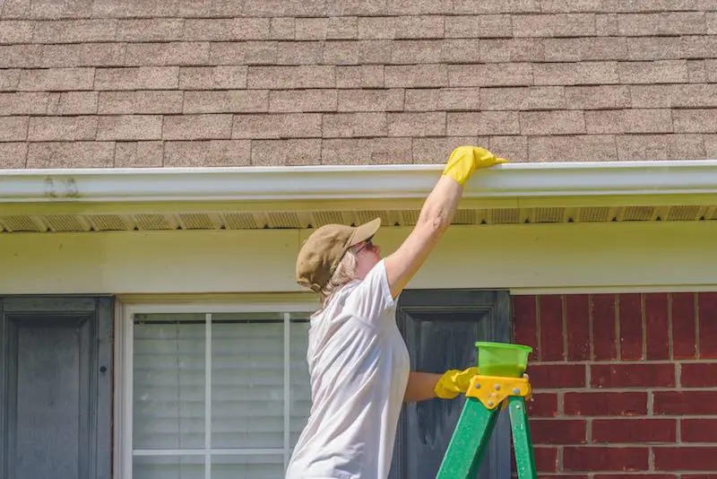 Woman on top of a ladder cleaning the gutter 