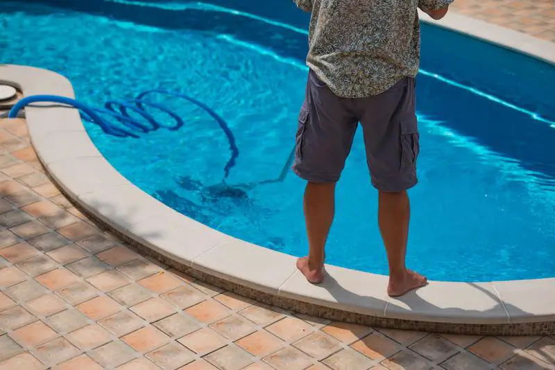 Man cleaning pool with a water vacuum cleaner