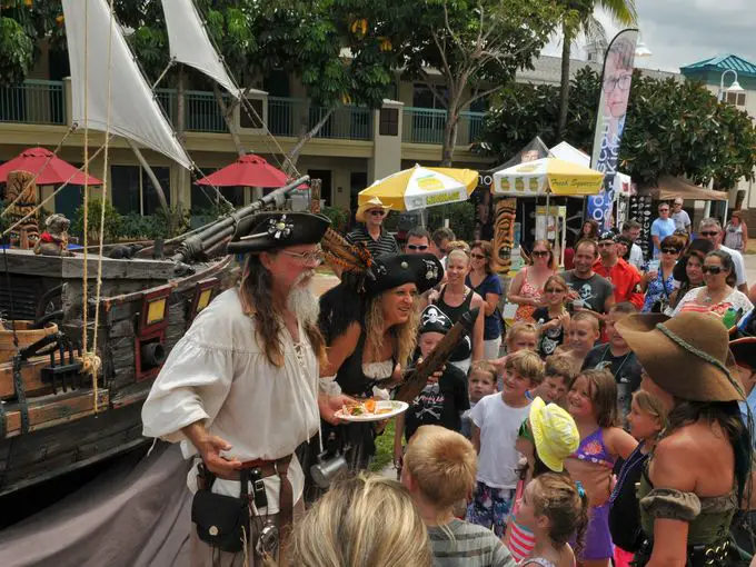 Crowds surrounding a man and woman dressed as pirates and standing in front of a small pirate ship