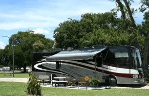 Large RV parked under a tree at the Orange Blossom KOA campground