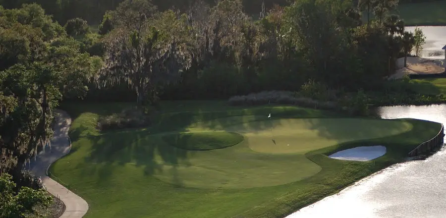 Golf course hole shaded by large trees covered with hanging spanish moss.