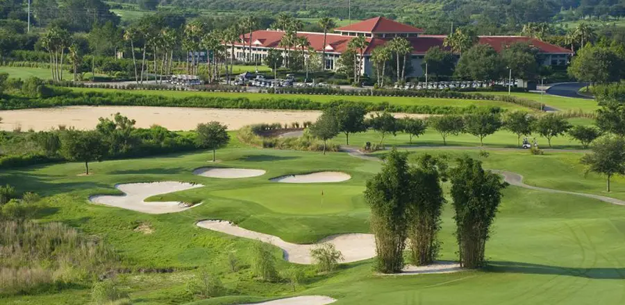 Golf course with sand traps surrounding a hole with a large red-roofed club house in the background.