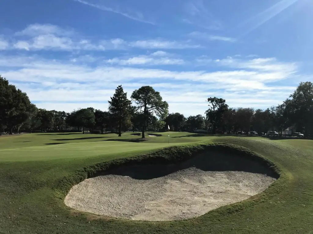 Golf course hole with oval-shaped sand trap in the foreground with golf green in background.