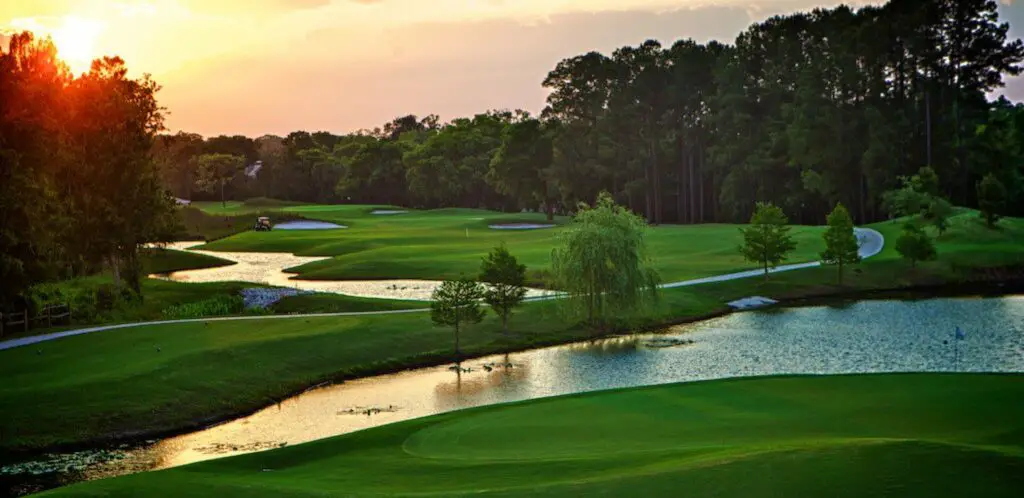 Golf course at sunrise with small streams running along the left side of the green with large trees lining the other side.