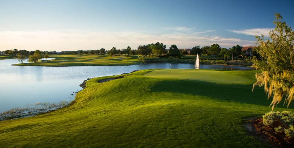 Golf course hole looking from fairway to green with large pond on left side of hole.